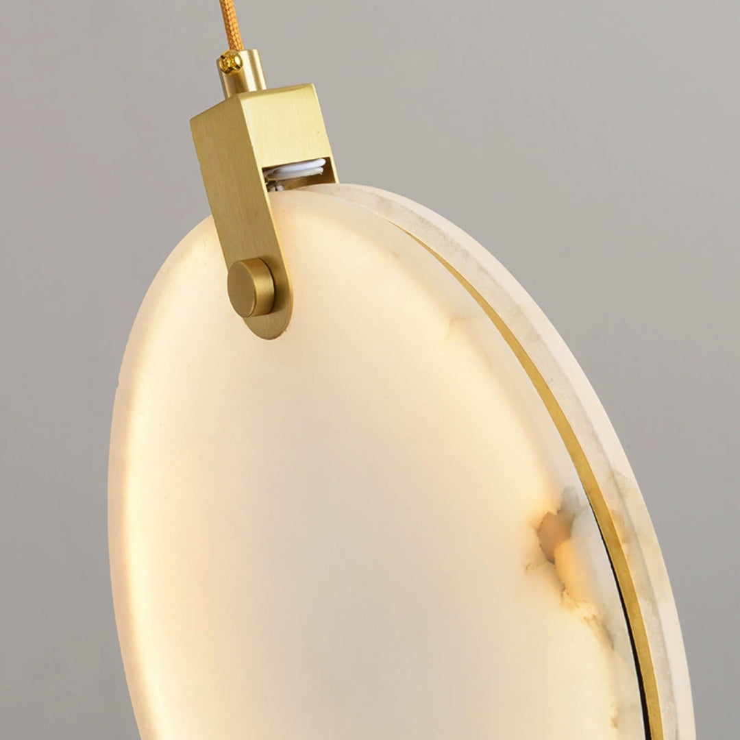 Close view of the brass hanger and the veined alabaster edge of one lit disc on this Clérachic pendant, on a grey backdrop.