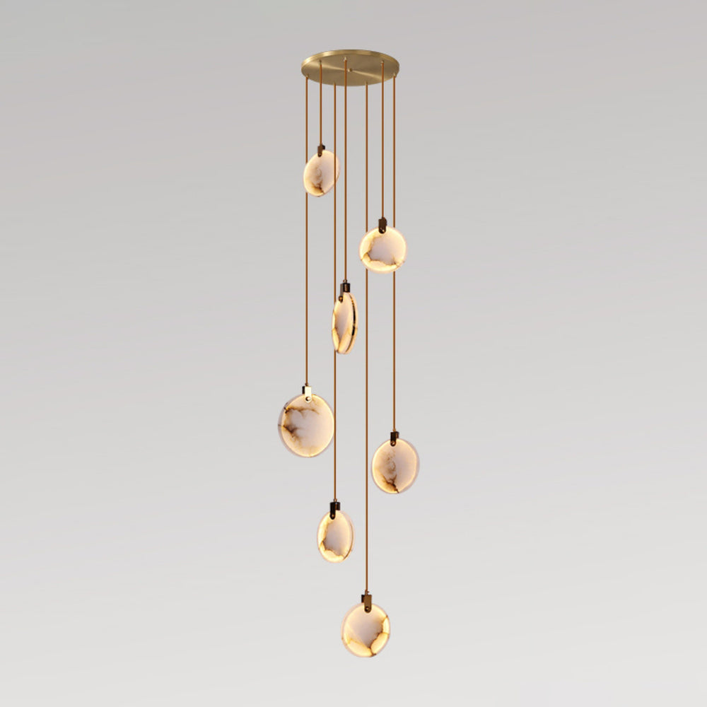 A Clérachic pendant cluster of seven alabaster discs at staggered heights from a gold canopy, on a soft grey backdrop.