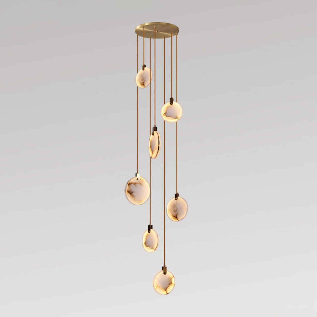 Alabaster discs of this Clérachic pendant hang at different lengths from a round gold canopy, lit warm against a pale grey backdrop.