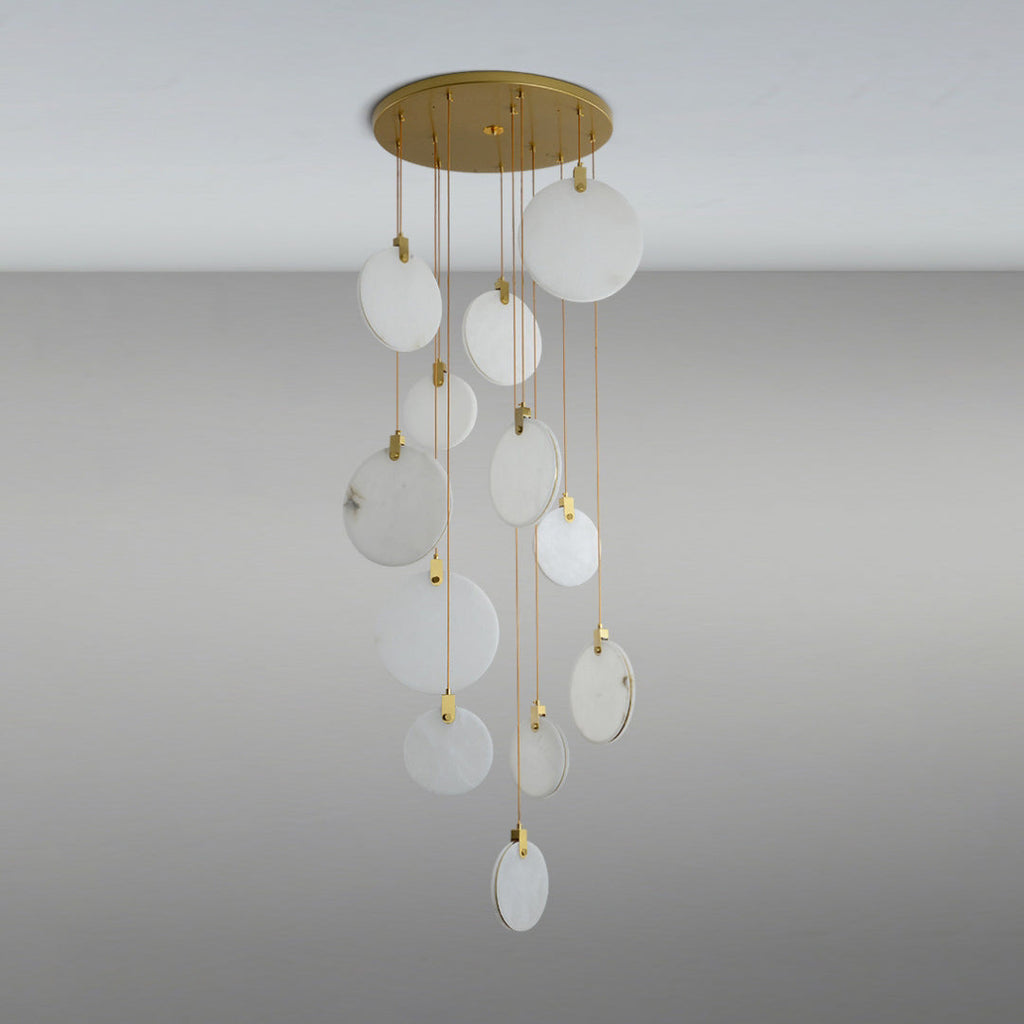 Unlit Clérachic alabaster disc pendants of different sizes hang from a round gold canopy, appearing pale and milky on a grey backdrop.