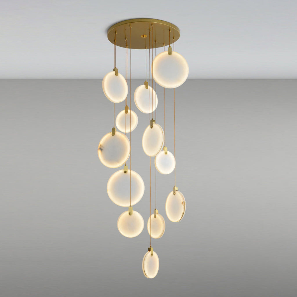 The same Clérachic alabaster discs lit up, glowing warm white at different heights from a round gold canopy on a grey backdrop.
