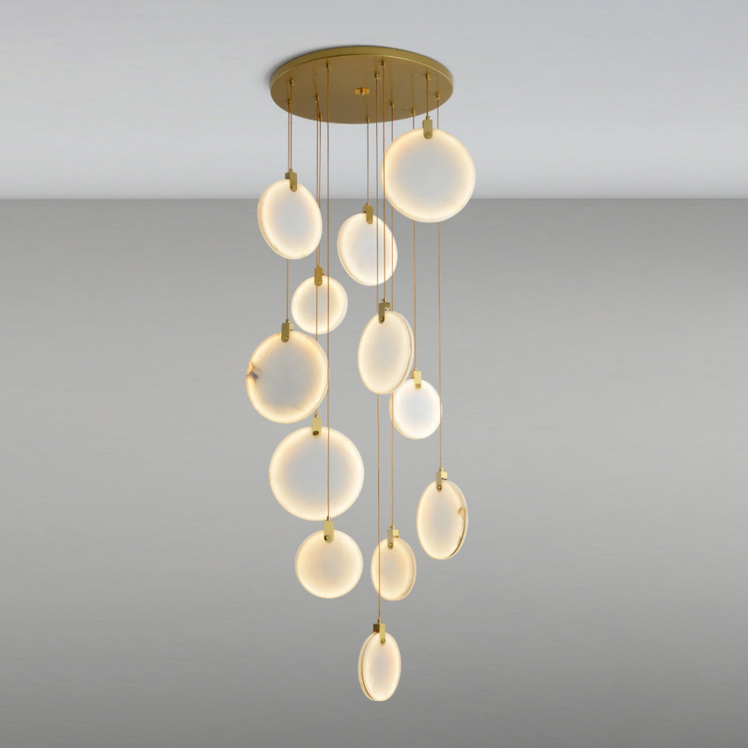 The same Clérachic alabaster discs lit up, glowing warm white at different heights from a round gold canopy on a grey backdrop.