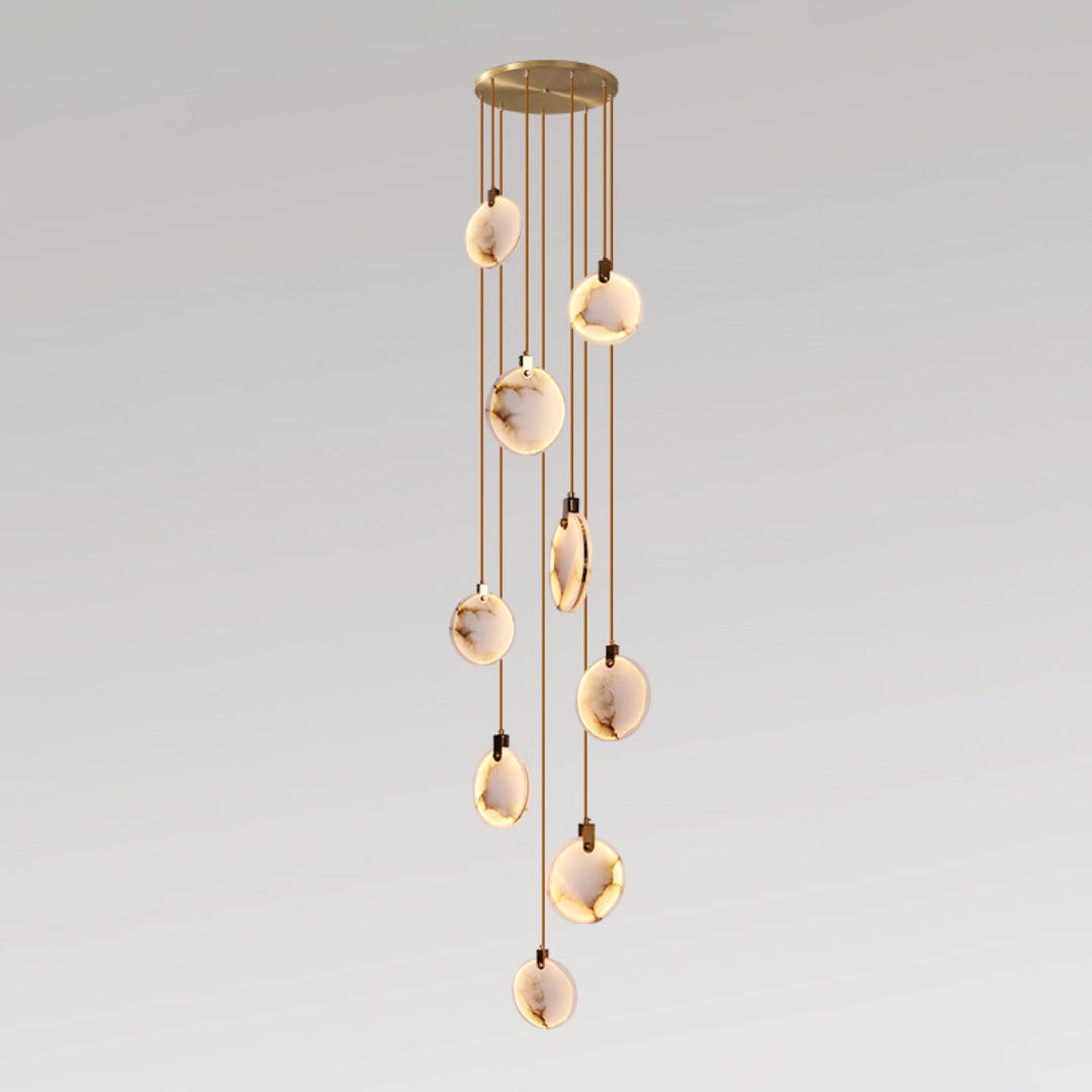 A Clérachic cluster of alabaster discs on tan cords in a loose column from a gold canopy, lit warm on a grey gradient backdrop.