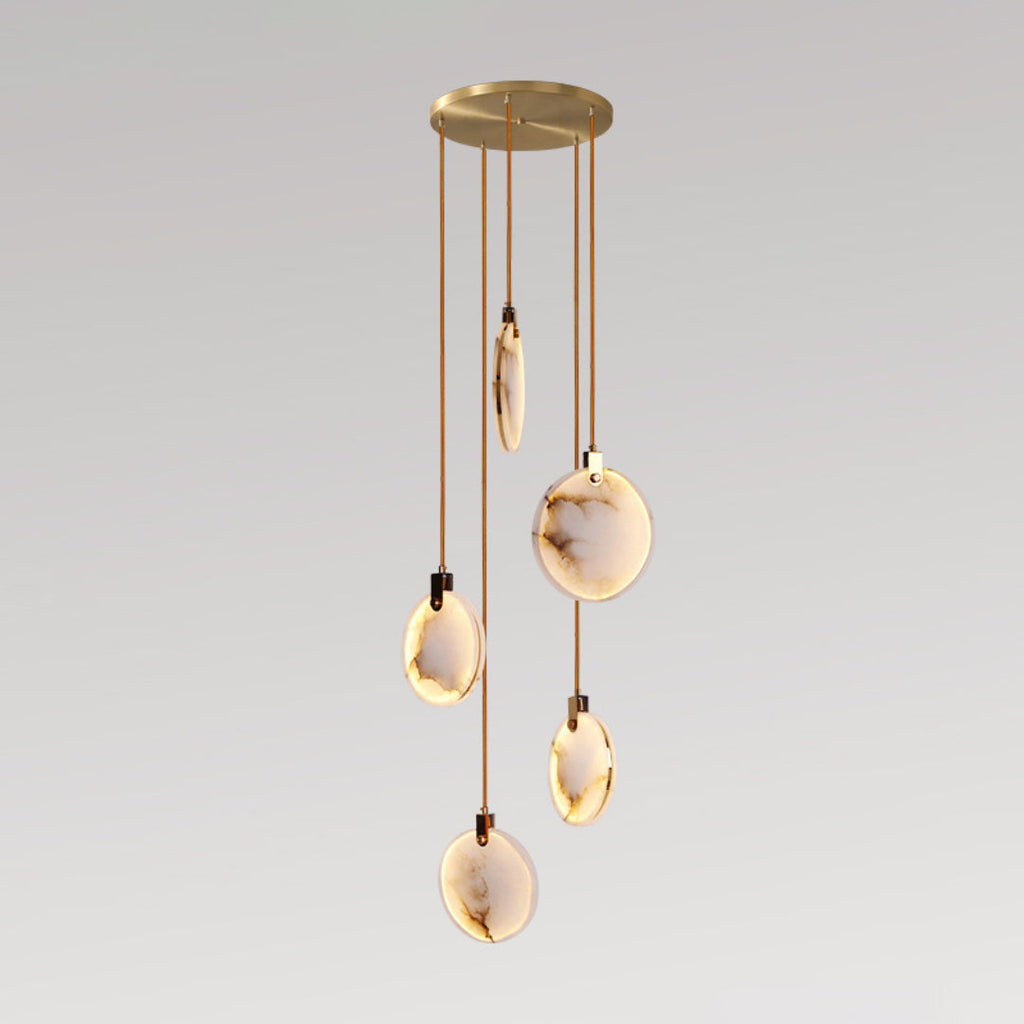 Five Clérachic alabaster disc pendants lit warm on cords of different lengths from a round gold canopy, on a grey backdrop.