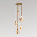 Five Clérachic alabaster disc pendants lit warm on cords of different lengths from a round gold canopy, on a grey backdrop.