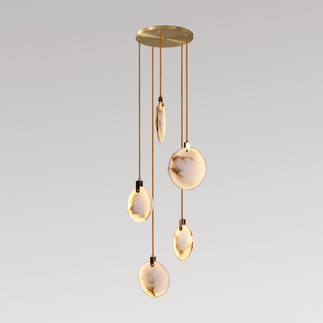 Five Clérachic alabaster disc pendants lit warm on cords of different lengths from a round gold canopy, on a grey backdrop.