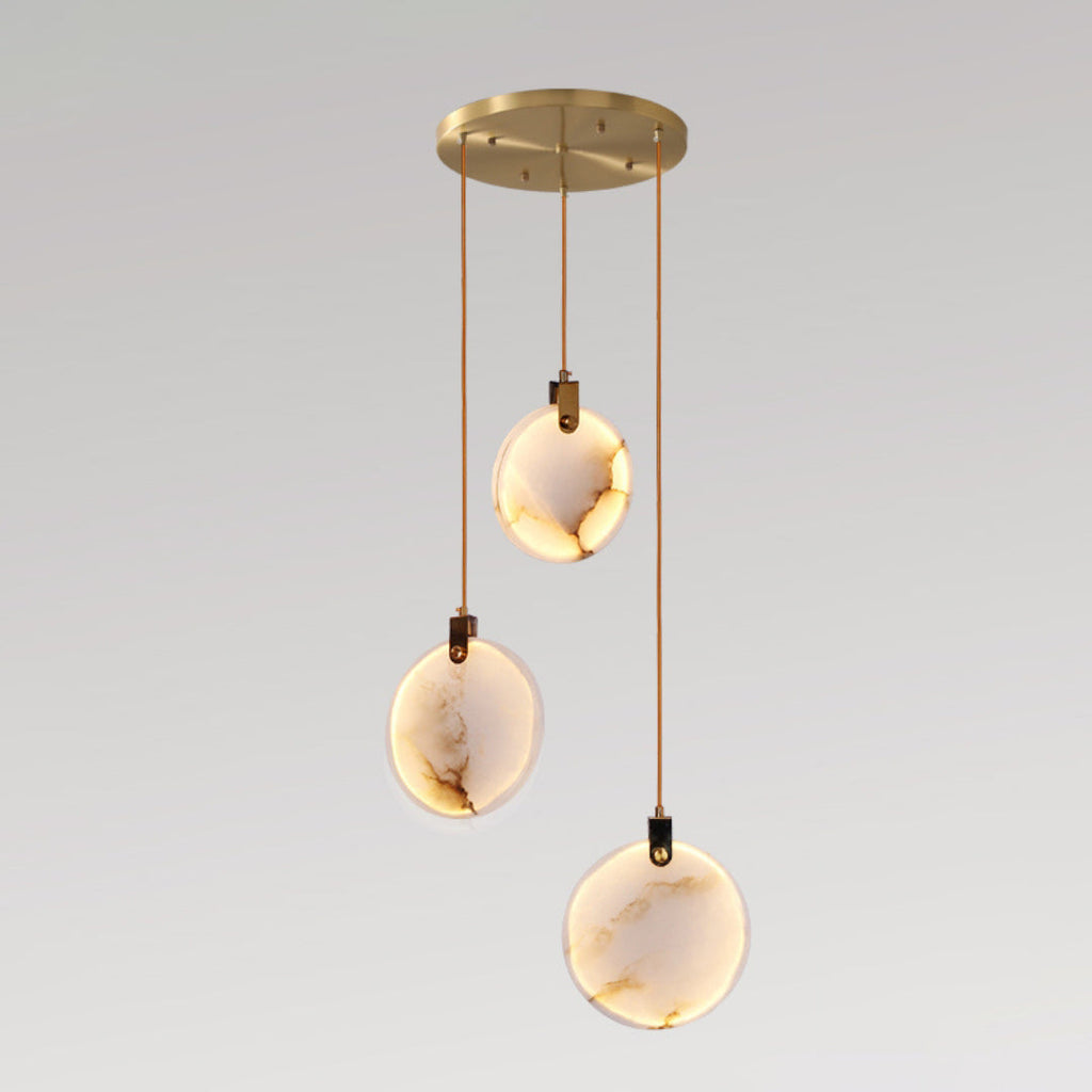 Three veined Clérachic alabaster disc pendants lit warm, hanging at different heights from a round gold canopy, on a grey backdrop.