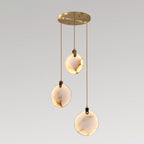 Three veined Clérachic alabaster disc pendants lit warm, hanging at different heights from a round gold canopy, on a grey backdrop.