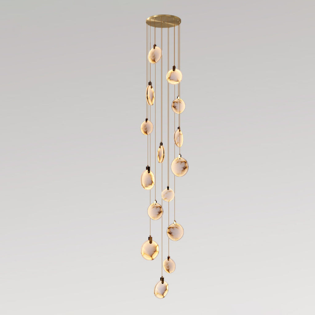 A tall Clérachic pendant cluster with many alabaster discs, lit warm, hanging in a slender column from a gold canopy.