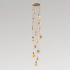 A tall Clérachic pendant cluster with many alabaster discs, lit warm, hanging in a slender column from a gold canopy.