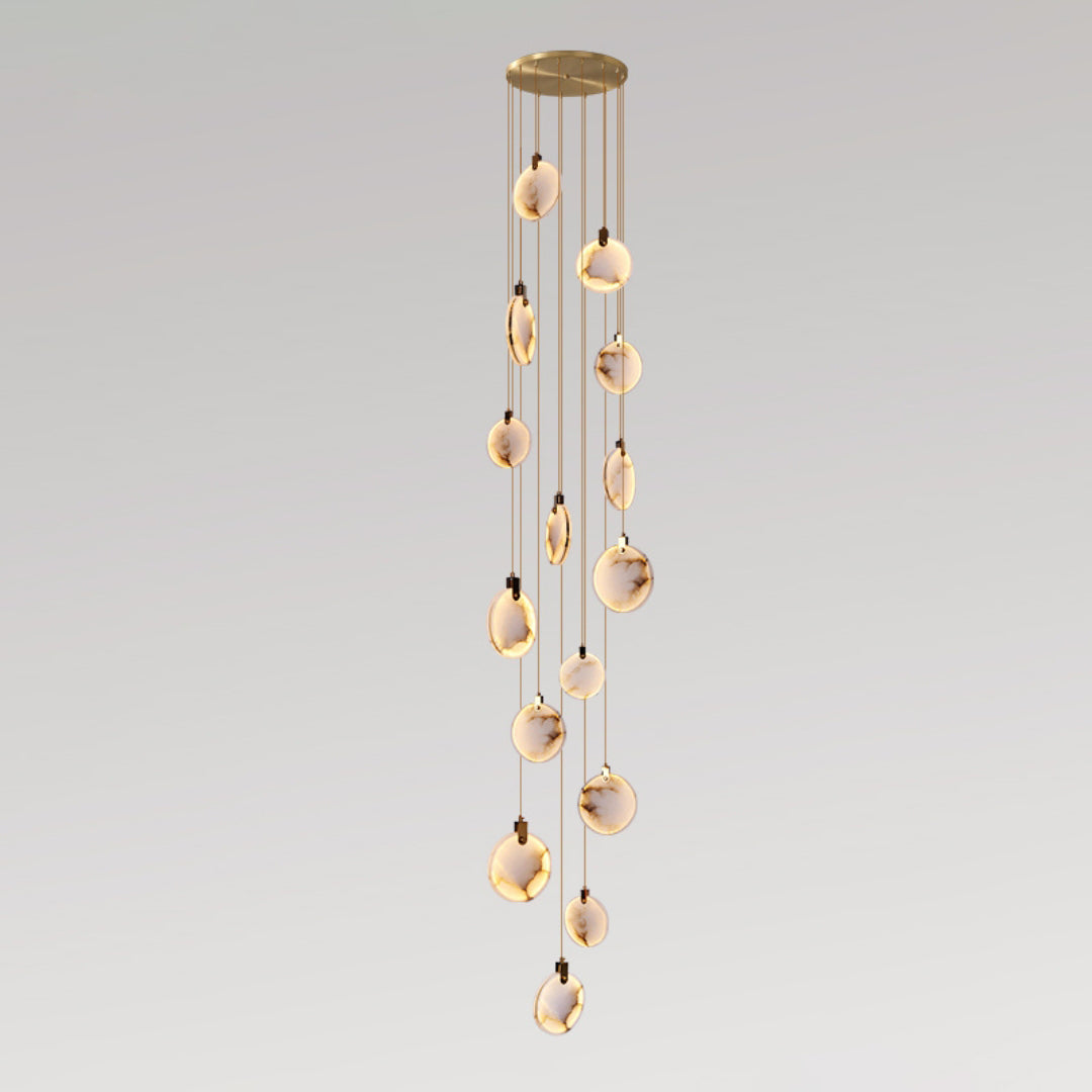 A tall Clérachic pendant cluster with many alabaster discs, lit warm, hanging in a slender column from a gold canopy.