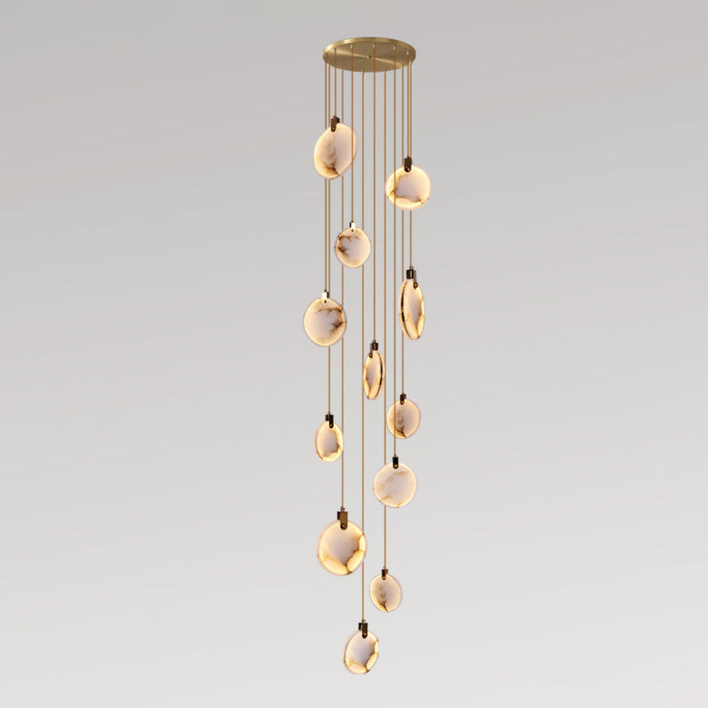 Clérachic alabaster disc pendants lit warm at staggered heights on tan cords from a round gold canopy, on a grey gradient backdrop.