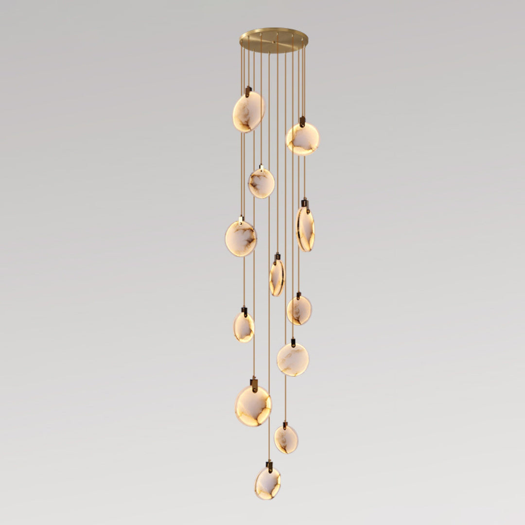 Clérachic alabaster disc pendants lit warm at staggered heights on tan cords from a round gold canopy, on a grey gradient backdrop.