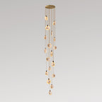 A very long column of small Clérachic alabaster discs on tan cords, lit warm and hanging from a gold canopy, on a grey backdrop.