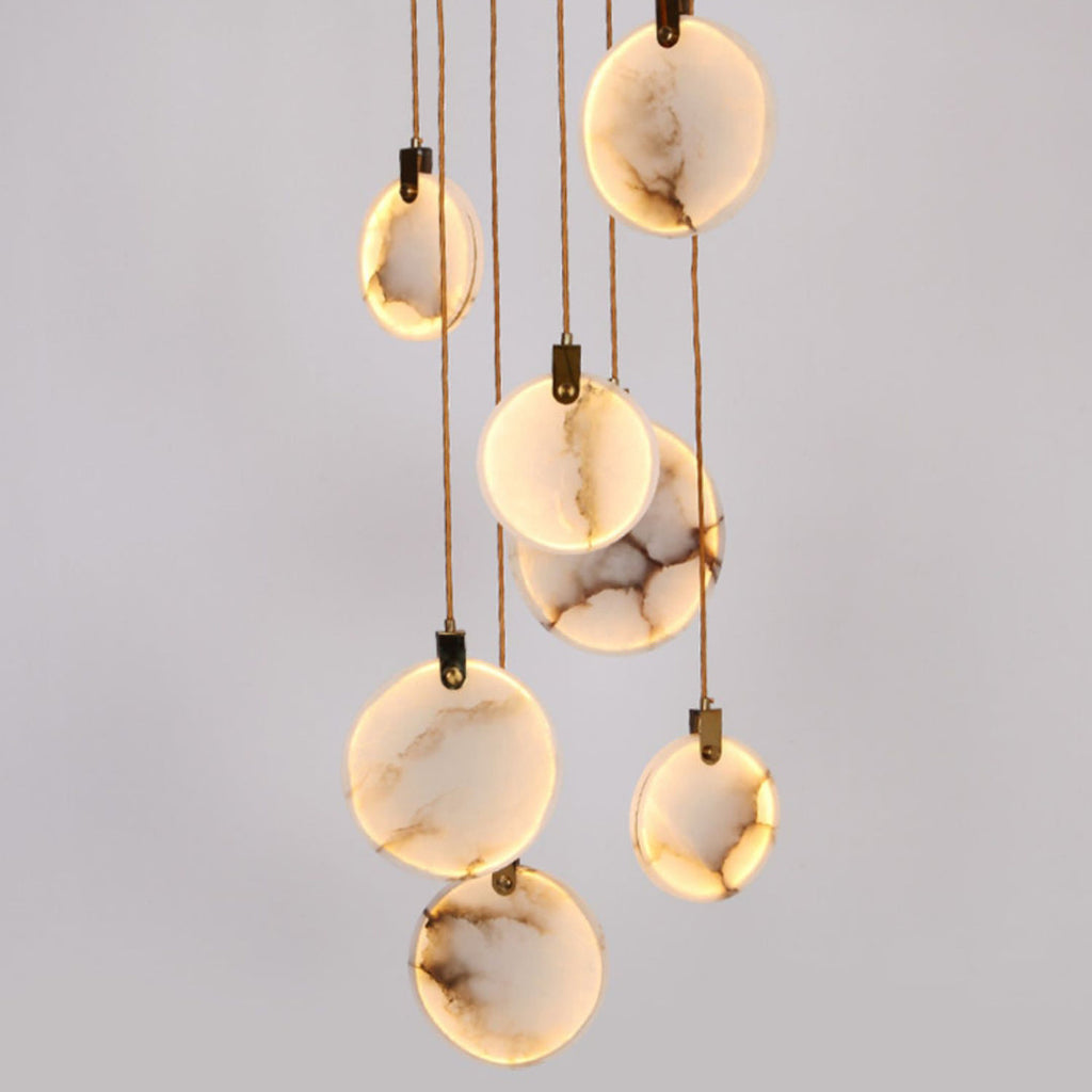 Close view of lit, veined alabaster discs hanging on tan cords from this Clérachic pendant, with dark hangers at the top of each.