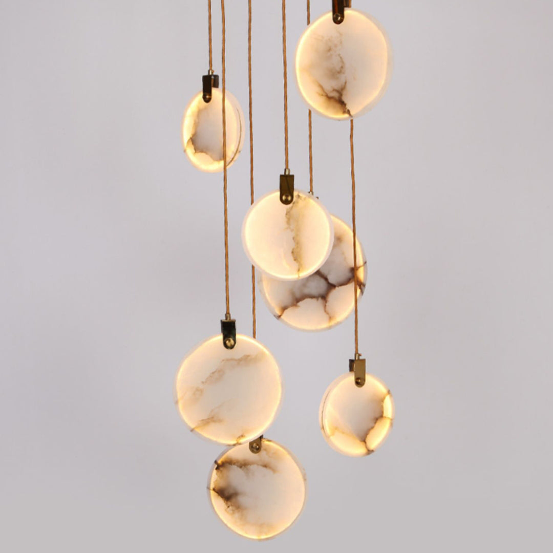 Close view of lit, veined alabaster discs hanging on tan cords from this Clérachic pendant, with dark hangers at the top of each.