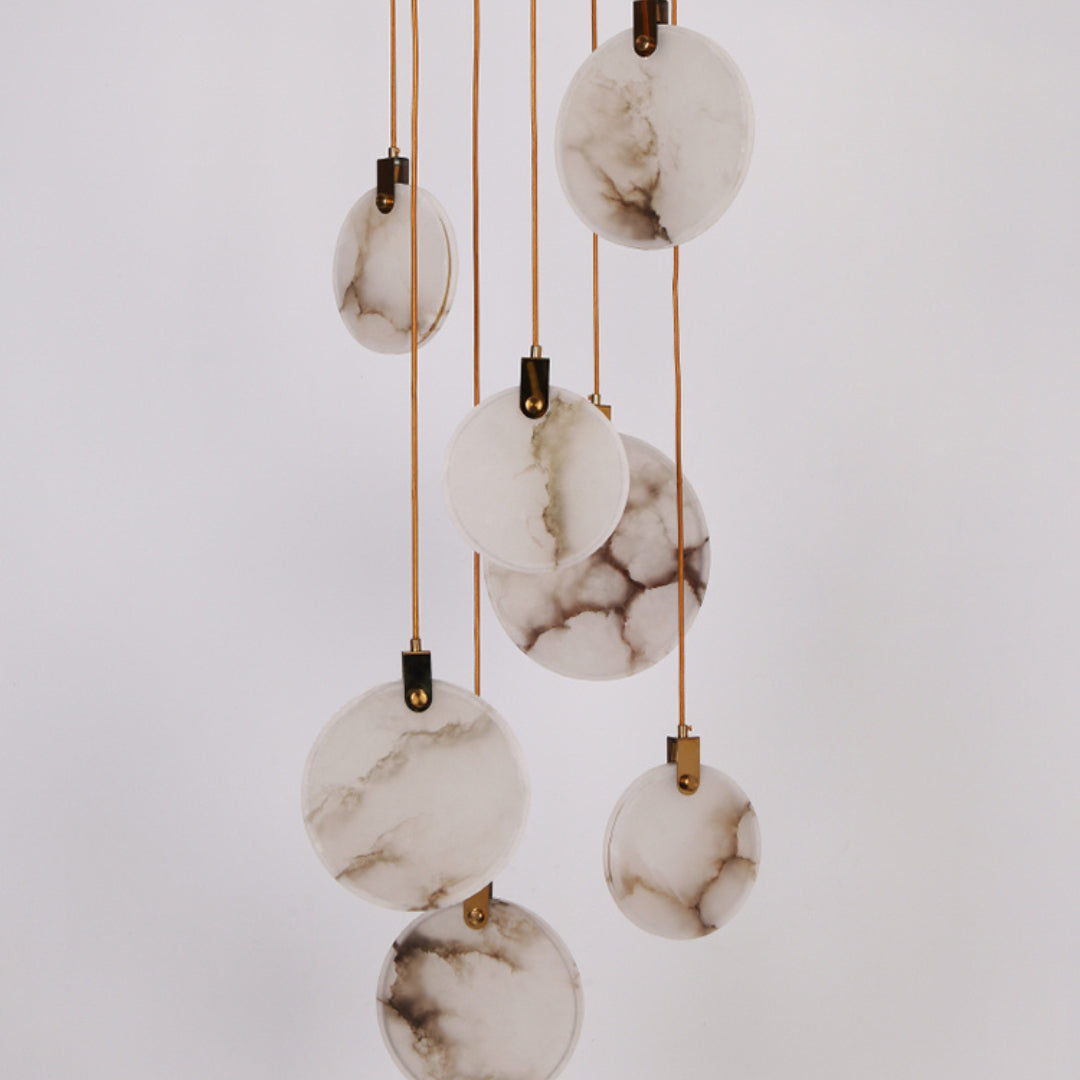Close view of unlit alabaster discs of this Clérachic pendant, showing grey and brown veining, on a pale lilac-grey backdrop.