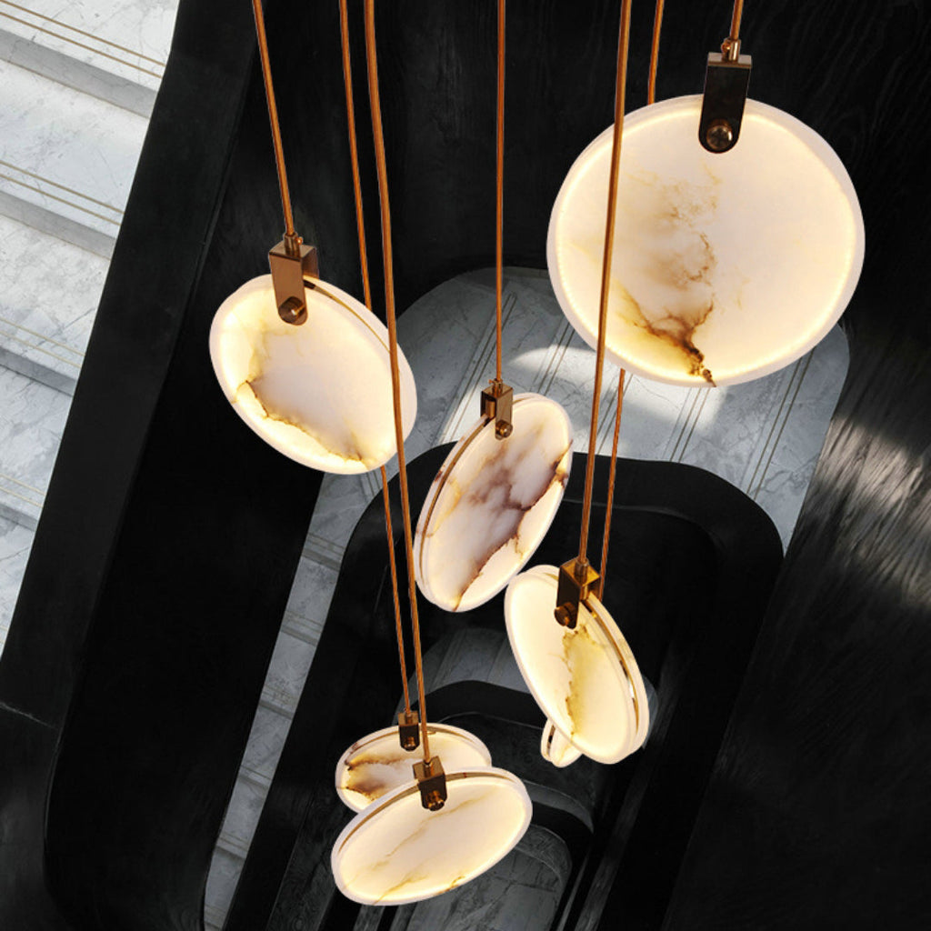 Looking down on five alabaster discs of this Clérachic pendant on tan cords, over a dark spiral stairwell.