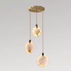 Three veined Clérachic alabaster disc pendants lit warm at different heights from a round gold canopy, on a pale grey backdrop.