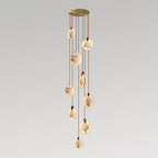 A Clérachic pendant cluster of nine alabaster discs on thin tan cords from a gold canopy, lit warm on a grey gradient backdrop.