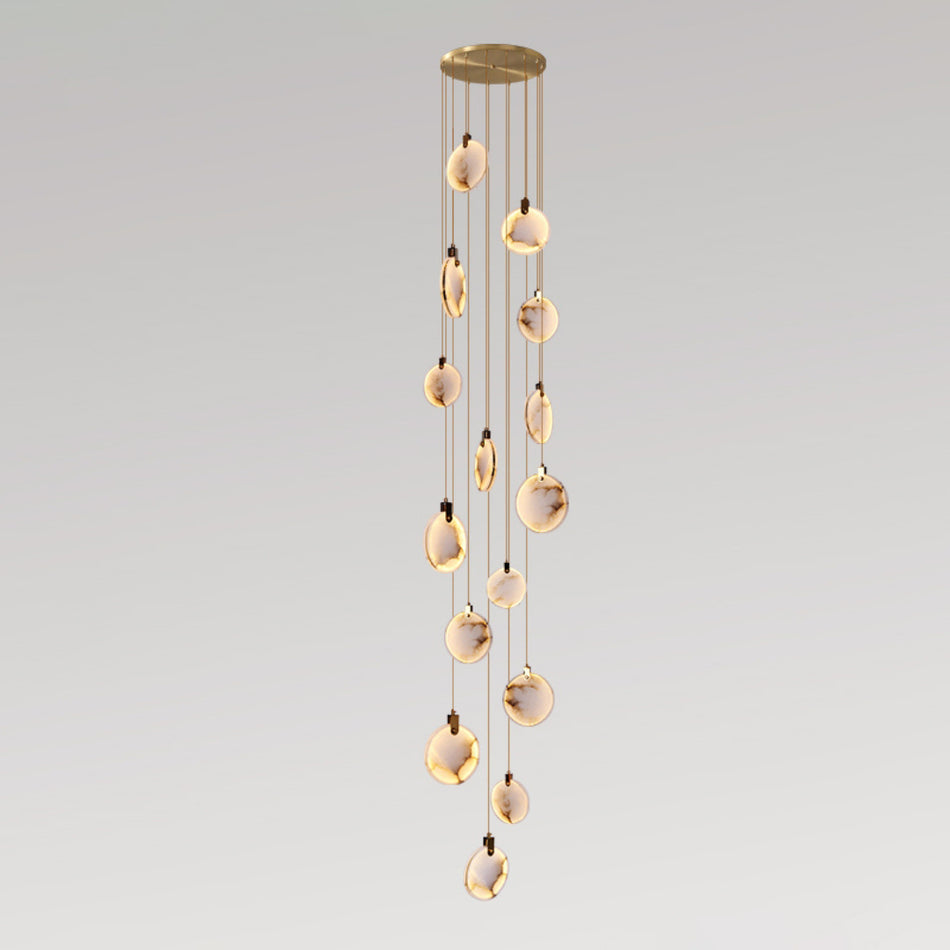 A tall Clérachic cluster of alabaster discs, lit warm, hanging in a slim column from a round gold canopy on pale grey.