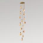 A tall Clérachic cluster of alabaster discs, lit warm, hanging in a slim column from a round gold canopy on pale grey.