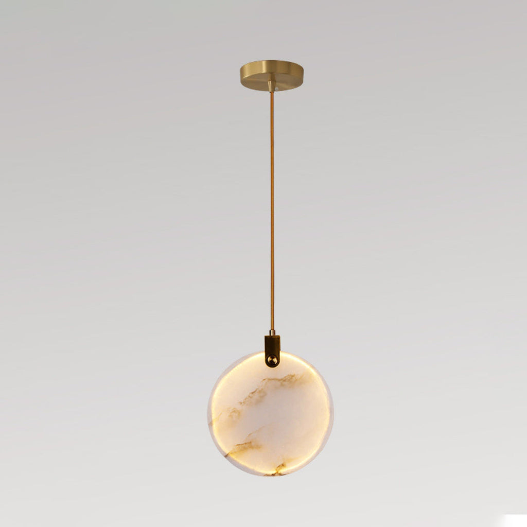 A single Clérachic alabaster disc pendant lit warm, on a brass rod and a small gold ceiling plate, against a grey backdrop.