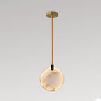 A single Clérachic alabaster disc pendant lit warm, on a brass rod and a small gold ceiling plate, against a grey backdrop.