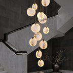 Lit Clérachic alabaster discs hang beside a stair of grey marble with a recessed handrail light, with a vase of branches below.