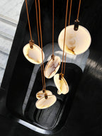 A top-down view of five Clérachic alabaster discs on tan cords with dark hangers, hanging over a black stairwell.