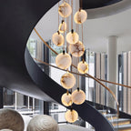Clérachic alabaster disc pendants hang in front of a black spiral staircase with a timber rail and glass walls behind.