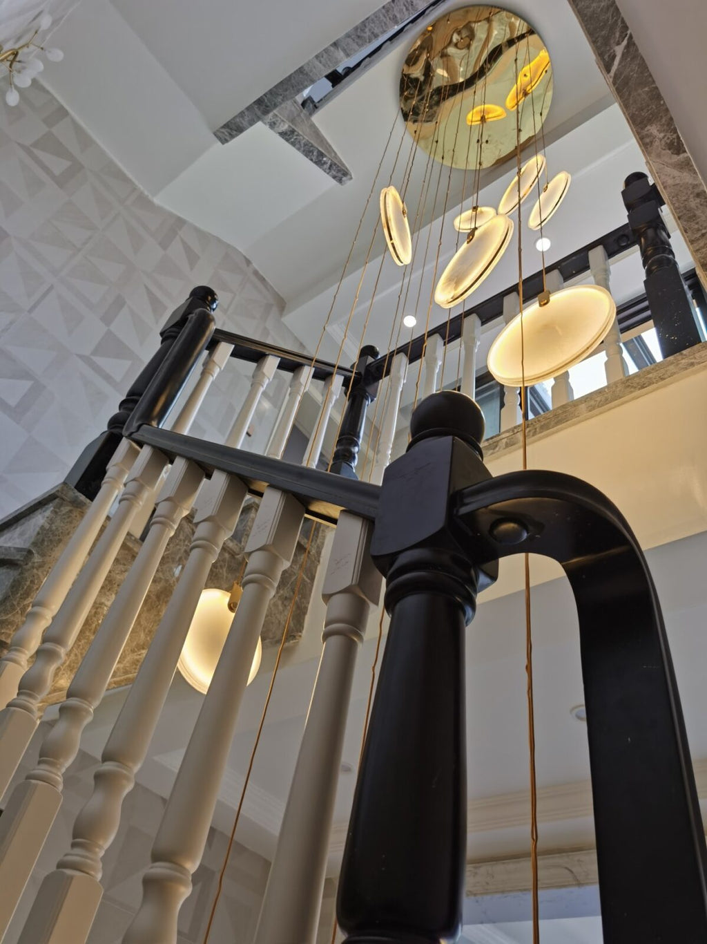 Looking up through white and black balusters at a Clérachic alabaster disc cluster and a round, mirror-finish ceiling plate.
