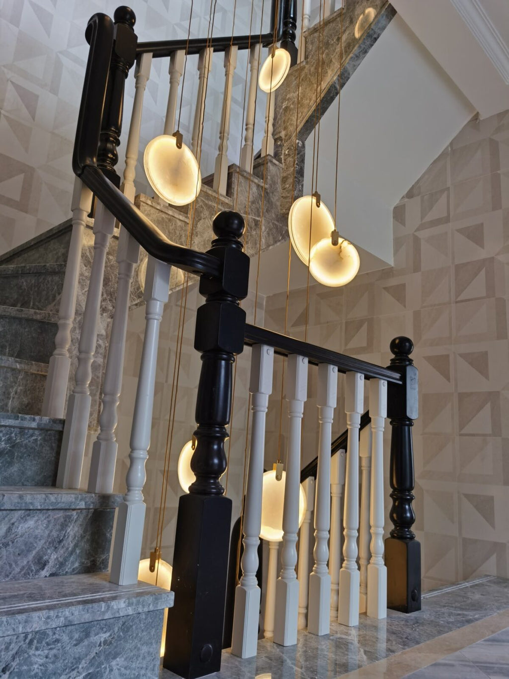 Clérachic alabaster discs glow above a stair with white balusters, black newel posts and grey marble steps.