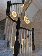 Clérachic alabaster discs glow above a stair with white balusters, black newel posts and grey marble steps.