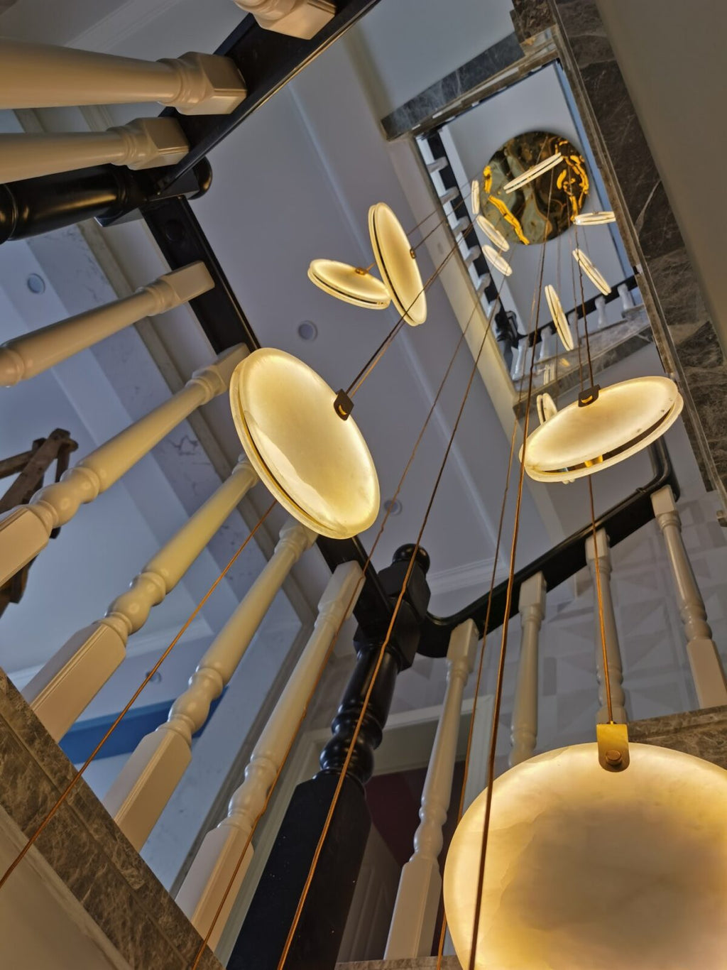 A wide-angle upward view of a stairwell, where lit Clérachic alabaster discs hang below a round gold ceiling plate.