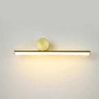Horizontal gold tube of this Clérachic wall light with a round gold disc above it, lit with a warm glow on a pale wall.