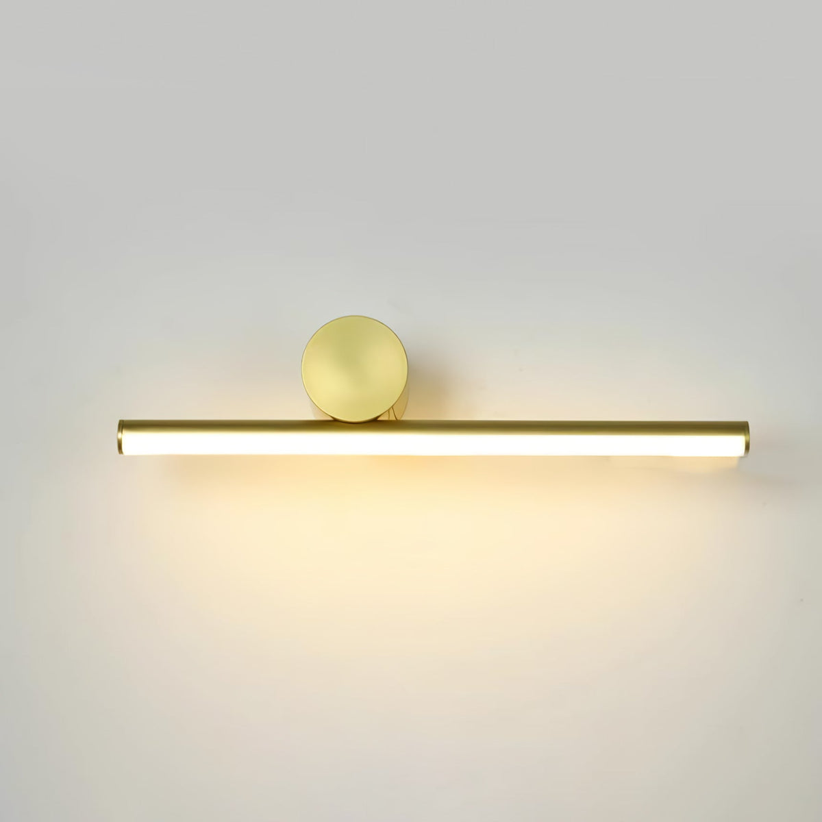Horizontal gold tube of this Clérachic wall light with a round gold disc above it, lit with a warm glow on a pale wall.
