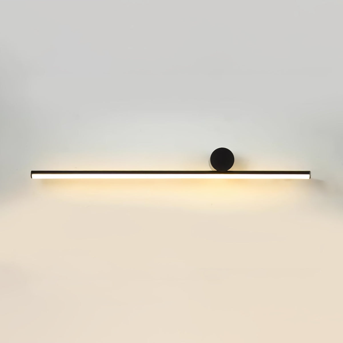 Long horizontal black tube of this Clérachic wall light with a small black disc, lit warmly on a pale wall.