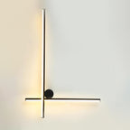Black Clérachic wall light with a long vertical tube crossed low by a horizontal tube and a black disc, lit warm on a pale wall.