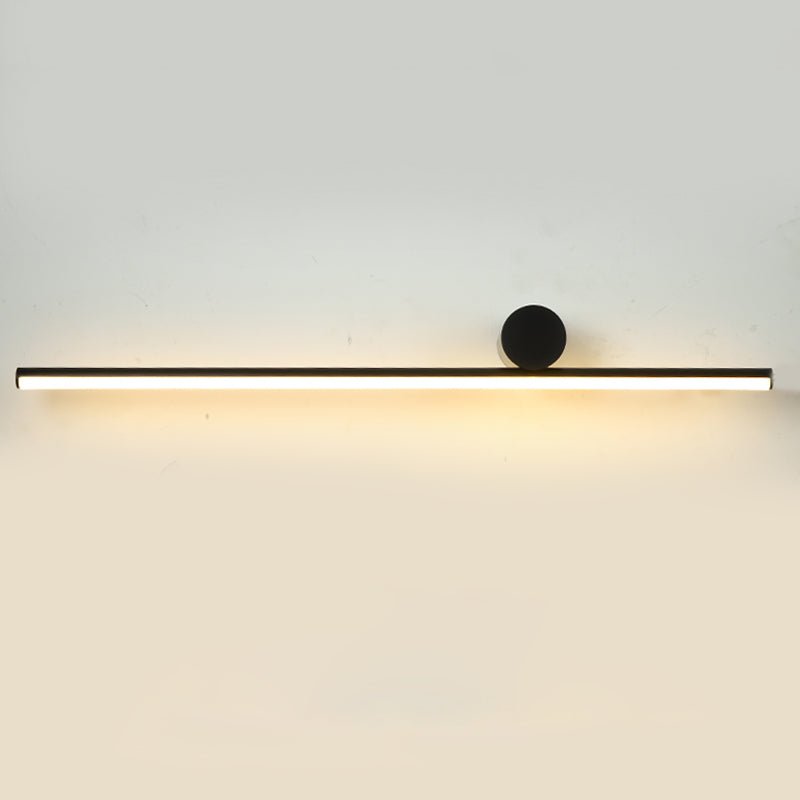 Long horizontal black tube of this Clérachic wall light with a small disc at the right, glowing warmly on a pale wall.