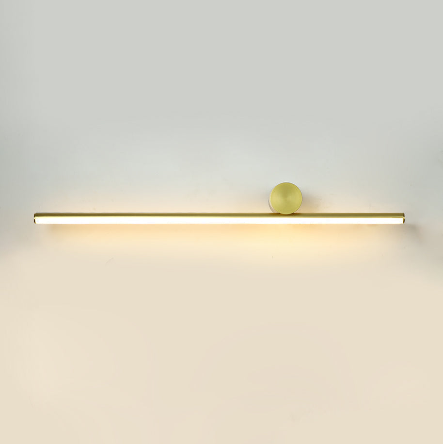 Slim horizontal gold tube of this Clérachic wall light with a small gold disc, giving a warm glow on a pale wall.