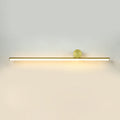 Slim horizontal gold tube of this Clérachic wall light with a small gold disc, giving a warm glow on a pale wall.