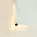 Black Clérachic wall light with a long vertical tube and a horizontal tube crossing low, with a small black disc, lit on a pale wall.