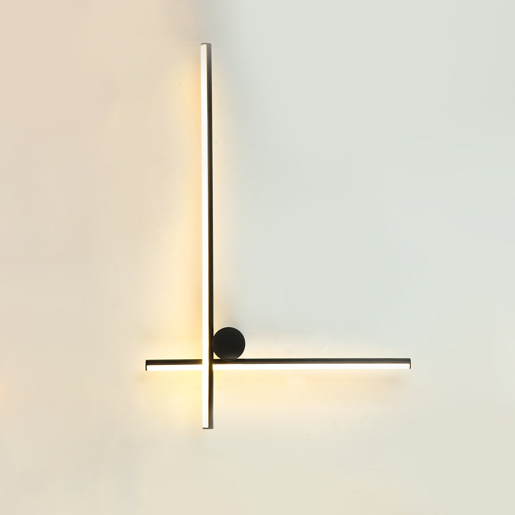 Black Clérachic wall light with a long vertical tube and a horizontal tube crossing low, with a small black disc, lit on a pale wall.