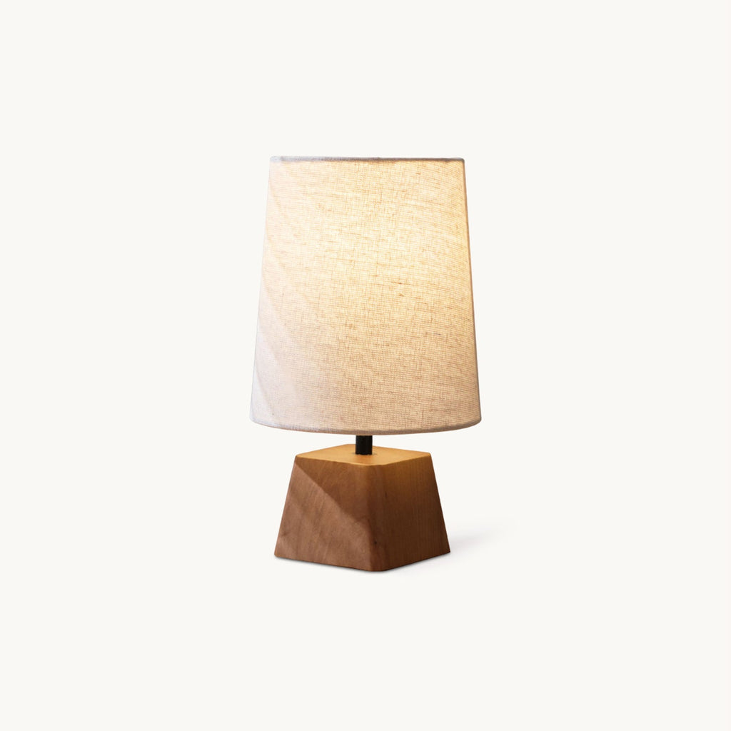 This Clérachic table lamp on a plain white backdrop, a linen drum shade above a faceted wooden base.