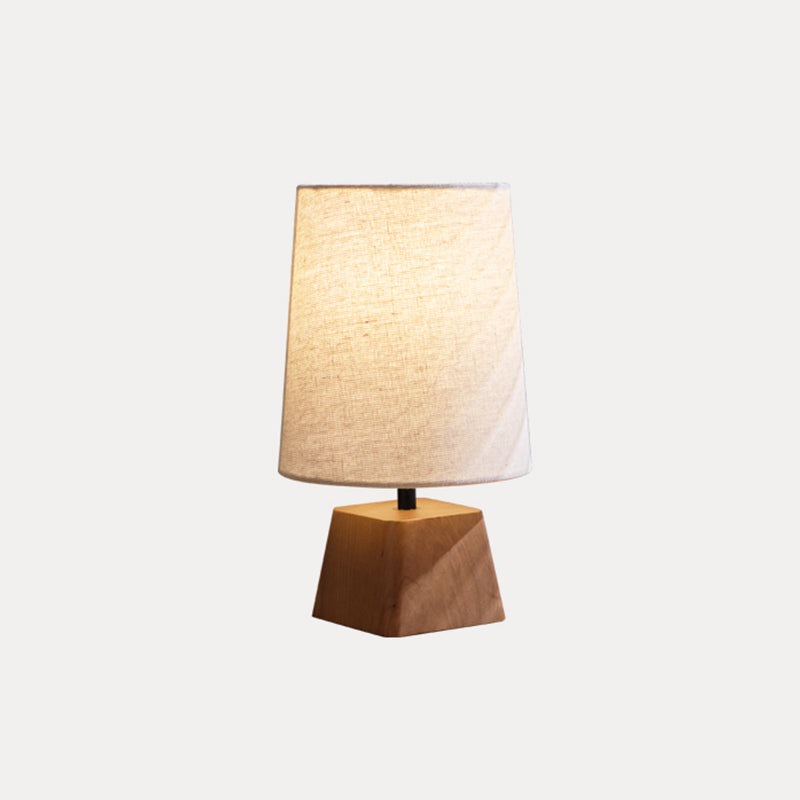 This Clérachic table lamp lit on a pale grey backdrop, a warm glow through the shade above its tapered wooden base.