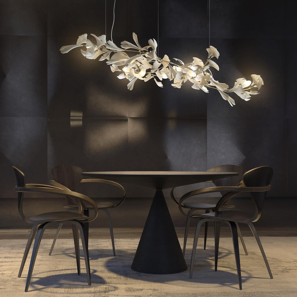 The Clérachic gingko chandelier lit above a round table with curved timber chairs in a dark room.