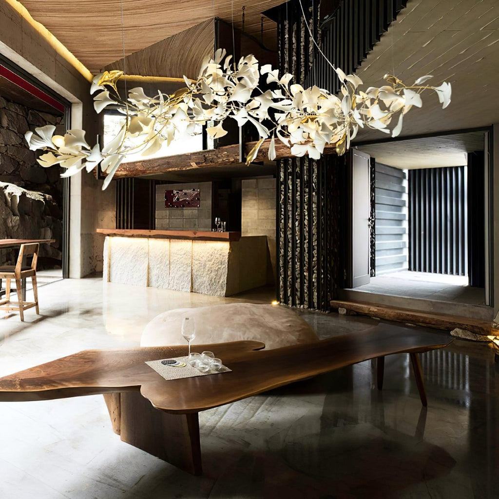 The Clérachic gingko linear chandelier lit above a live-edge timber table in a stone-walled room.