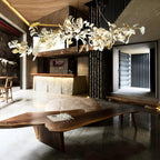 The Clérachic gingko linear chandelier lit above a live-edge timber table in a stone-walled room.