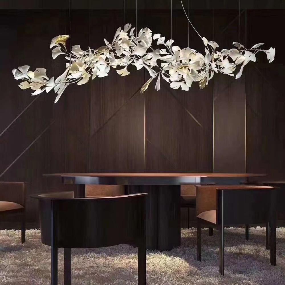 Clérachic gingko linear chandelier lit over a dark dining table against timber panelling.